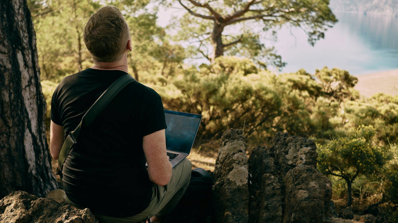 A photograph of a person using a laptop in a forest.