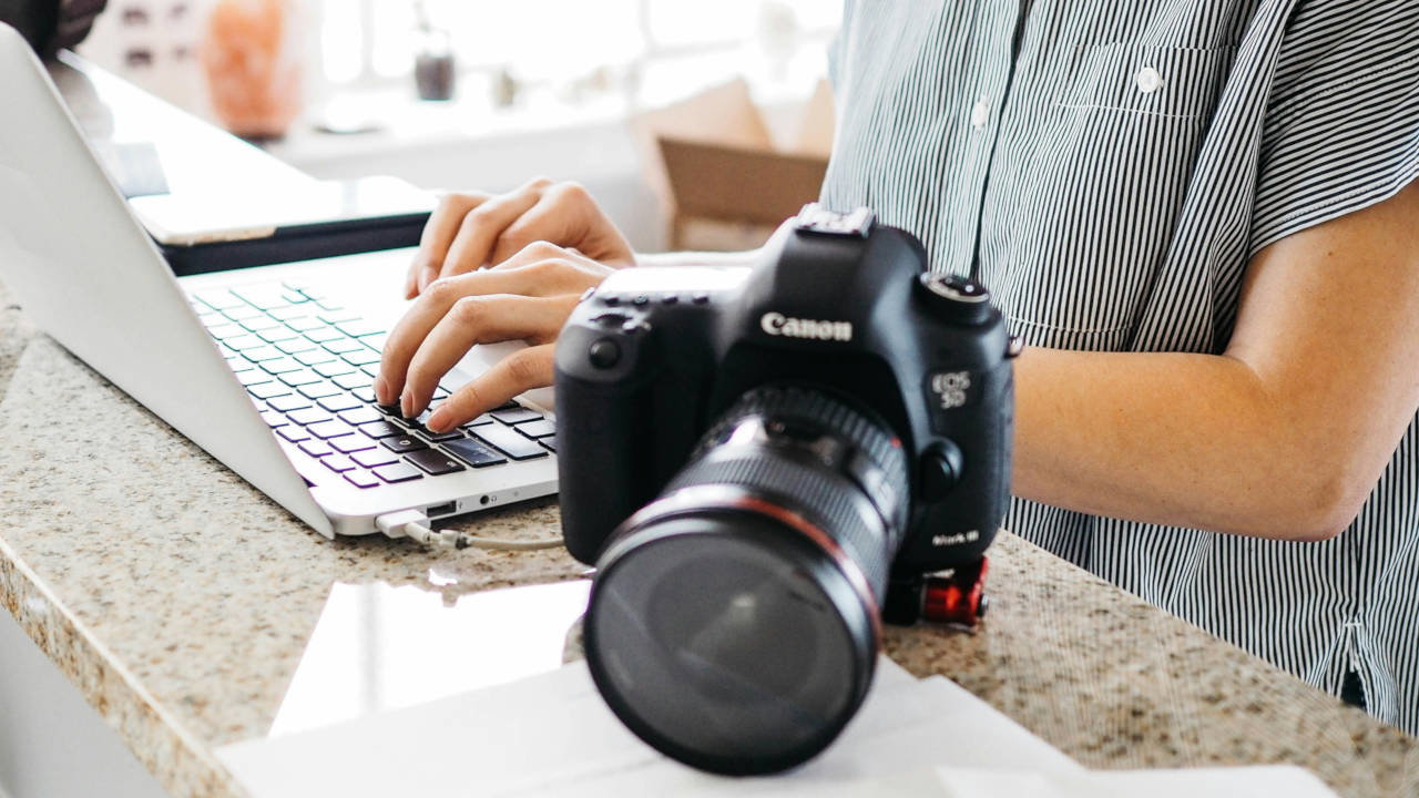 A photograph of a person typing on a laptop beside a SLR camera.