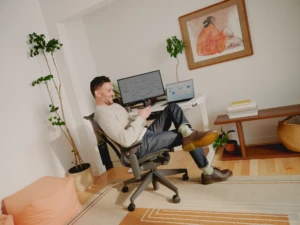 Man sitting near a desk with monitor and laptop