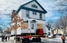 White Victorian house with blue trim on a trailer being moved during winter.