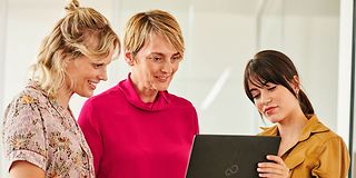 Image of three women, looking in a laptop and discussing.