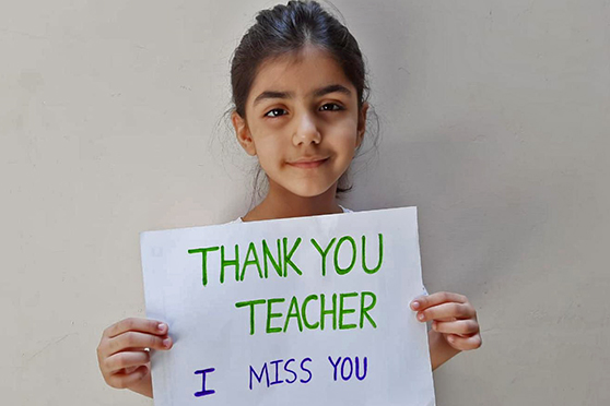 A young girl from Pakistan holding a sign which reads "Thank you teacher I miss you"
