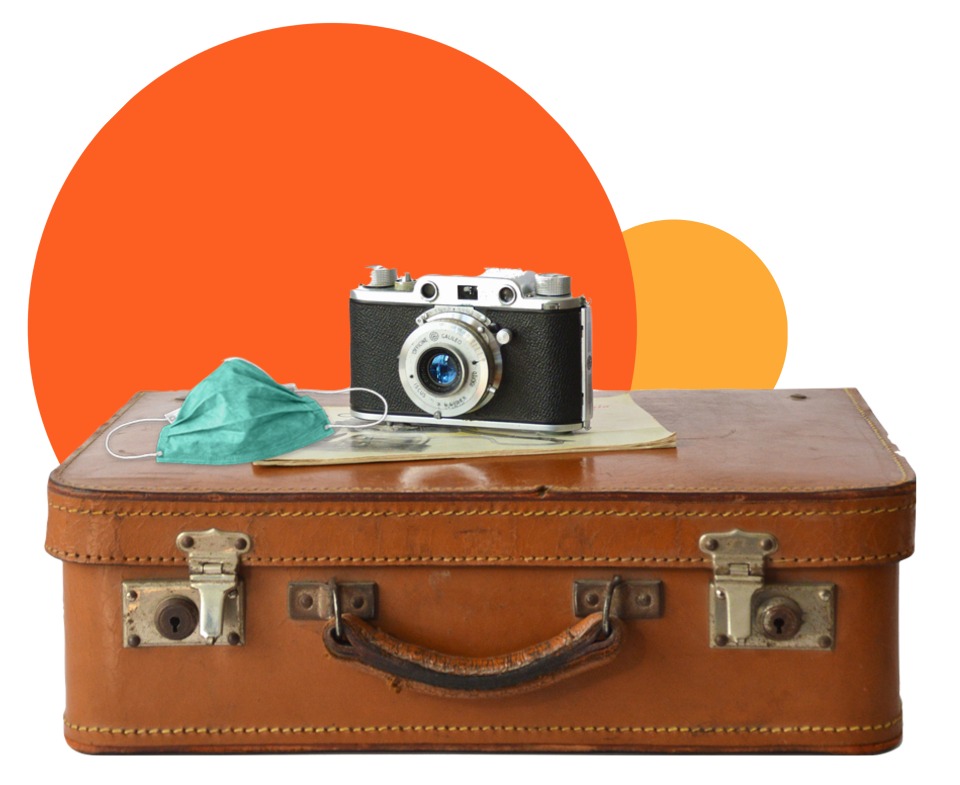 Photo camera, notebook and a face mask over a suitcase