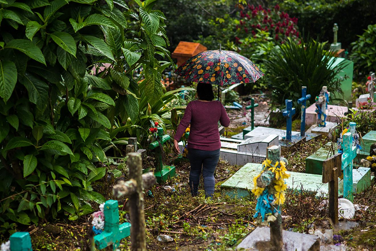 A woman with an umbrella walks among the graves in a cemetery.